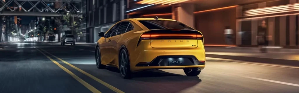 The image shows a yellow Toyota Prius driving at night on a city street.